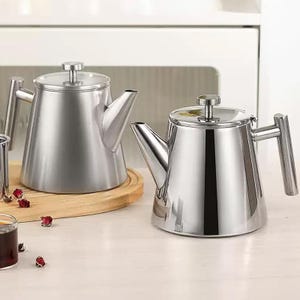 May include: Two stainless steel teapots with a modern design. Each teapot has a conical body, a spout, and a handle. The teapots are sitting on a wooden surface. The teapots are made of shiny, brushed metal.