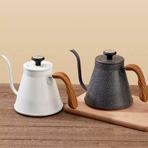 Op de afbeelding: Twee zwanenhalsketels met houten handvatten. Eén is wit, de andere is donkergrijs met een gespikkeld patroon. Beide hebben een zwart deksel met een thermometer. De ketels zijn ontworpen voor pour-over koffie.