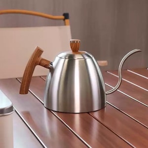 Peut inclure: Une bouilloire à col de cygne en acier inoxydable avec une poignée et un bouton de couvercle en bois. La bouilloire a un long bec courbé pour un versement précis. Le design est moderne et minimaliste, adapté au brassage du café.