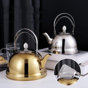 Peut inclure: Deux théières en acier inoxydable, une dorée et une argentée, avec des poignées arquées et des becs verseurs. La théière dorée est à gauche et la théière argentée à droite. Un petit infuseur à thé rond en acier inoxydable est dans le coin inférieur droit.