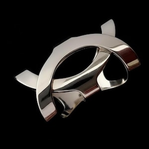 Könnte beinhalten: Eine polierte silberfarbene Metallskulptur mit geometrischem Design. Die Skulptur hat gebogene und eckige Elemente, die das Licht vor einem schwarzen Hintergrund reflektieren. Das Stück hat eine moderne, abstrakte Ästhetik.
