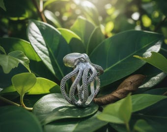 Peut inclure: Une bague argentée en forme de poulpe avec des tentacules détaillés et une tête texturée. La bague est posée sur un fond de feuilles vertes luxuriantes, créant une esthétique inspirée de la nature. Le design de la bague est complexe et accrocheur.