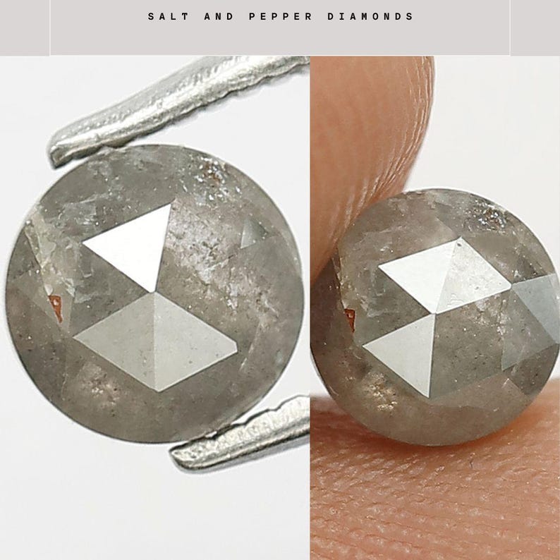 Op de afbeelding: Twee ronde zout- en peperdiamanten worden getoond. De diamanten zijn grijs met witte geometrische facetten. De diamanten worden vastgehouden door een pincet en een vinger. De tekst "SALT AND PEPPER DIAMONDS" staat bovenaan.