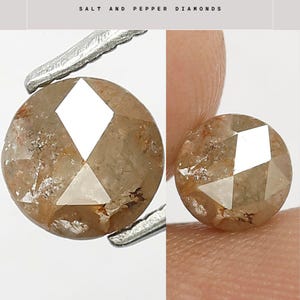 Op de afbeelding: Twee ronde zout- en peperdiamanten. De diamanten zijn lichtbruin met witte facetten. E&eacute;n wordt vastgehouden door een pincet, de andere door een vinger. De tekst "SALT AND PEPPER DIAMONDS" staat bovenaan.