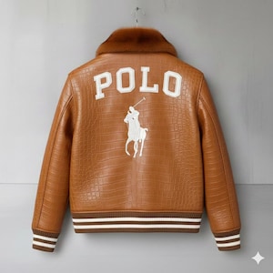 Puede incluir: Chaqueta de cuero marrón con cuello de piel sintética. La parte trasera de la chaqueta presenta la palabra "POLO" en letras blancas en bloque sobre una imagen bordada en blanco de un jugador de polo a caballo. La chaqueta tiene un patrón texturizado.