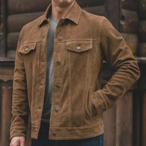 May include: A brown suede jacket with a button-up front, two chest pockets, and two side pockets. The jacket has a classic collar and long sleeves. The jacket is a medium brown color and appears to be made of soft suede material.