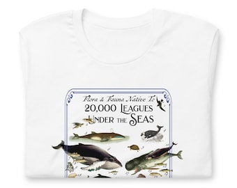 Puede incluir: Una camiseta blanca con un estampado gráfico de borde azul titulado Flora & Fauna Native To 20,000 LEAGUES UNDER THE SEAS. La ilustración muestra varios animales marinos, incluyendo ballenas, una foca y una tortuga, cada uno con un número.
