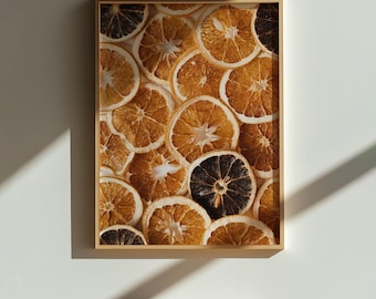 May include: A framed print featuring a close-up of dried orange slices. The slices vary in color from light orange to dark brown, with a natural, textured appearance. The artwork is set against a white background, with a wooden frame.