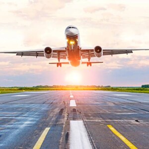 Puede incluir: Un avión comercial despegando de una pista al atardecer. La aeronave se recorta contra el sol brillante, con sus motores y tren de aterrizaje visibles. La pista está marcada con líneas amarillas y blancas.