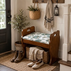 May include: A wooden entryway bench with a floral patterned cushion in shades of teal and white. The bench features side handles and an open base containing a woven basket with a cream-colored fringed throw blanket inside.