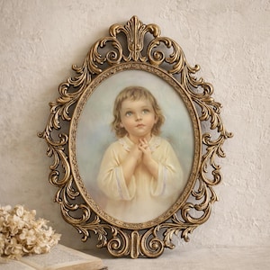 May include: An oval-shaped, antique-style picture frame with a gold finish. The frame surrounds a portrait of a child with light hair and blue eyes, dressed in a yellow garment. The frame has ornate, swirling details.
