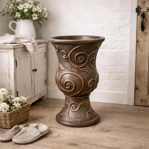 May include: A tall, brown decorative urn with a pedestal base. The urn features an embossed swirling leaf and scroll design. The urn is made of a durable material and is suitable for indoor or outdoor use. The urn is approximately 30 inches tall.