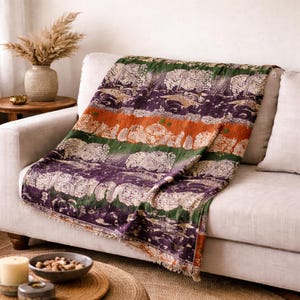 May include: A colorful throw blanket draped over a light-colored sofa. The blanket features a pattern of purple, green, and orange stripes with a textured design. The throw has a fringed edge and adds a decorative element to the living room.