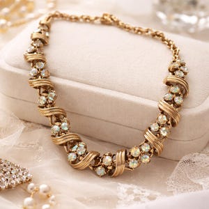 May include: A gold-toned necklace with iridescent, round gemstones and a twisted metal design. The necklace is displayed on a white surface, showcasing its intricate details and vintage style. The jewelry piece is a statement accessory.