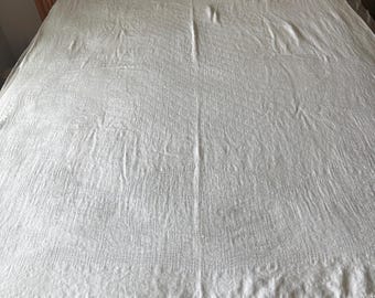 May include: A white, textured bedspread with a woven pattern, draped over a bed. The bedspread has a rectangular shape and covers the entire bed. The bed frame is visible at the top of the image.
