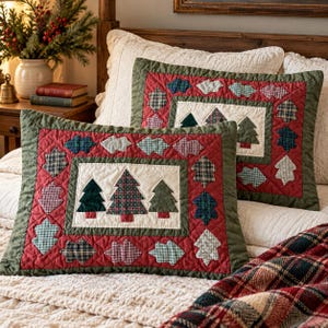 May include: Two rectangular quilted pillows featuring a central cream-colored panel with three appliquéd fabric Christmas trees. The border is red with a green trim, decorated with a repeating pattern of small, multi-colored plaid fabric leaves.