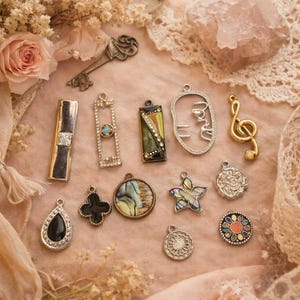 May include: A collection of various pendants and charms, including a key, a treble clef, and several geometric and floral designs. The charms are in gold, silver, and black, with accents of gemstones and abalone shell, arranged on a pink surface.