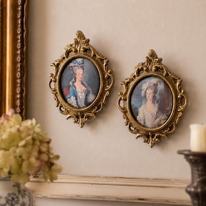 May include: Two antique gold-colored oval frames with portraits of women in period clothing. The frames are ornate with detailed scrollwork. The portraits feature women in blue and white dresses.