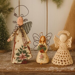 May include: Three decorative angel figurines. The largest angel has a cream-colored dress with floral patterns and metal wings. The middle angel holds a bouquet. The smallest angel is crocheted.