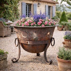 May include: A large, weathered metal planter filled with pink and purple flowers. The rusty brown planter has decorative crescent moon and star cutouts, and is supported by curved legs. The planter is outdoors, in a garden setting.