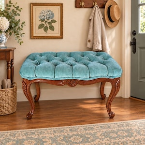 May include: A rectangular bench featuring a tufted, light blue velvet cushion seat. The base is constructed from dark brown wood with four curved legs, each displaying intricate carved floral details along the frame and the apron of the seat.