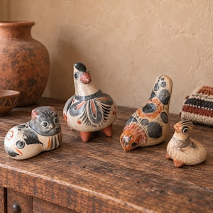 May include: Four hand-painted ceramic animal figurines featuring cream-colored bases with intricate black and terracotta-colored floral and geometric patterns. The collection includes a cat-like figure, two bird-shaped sculptures, and a small chick.