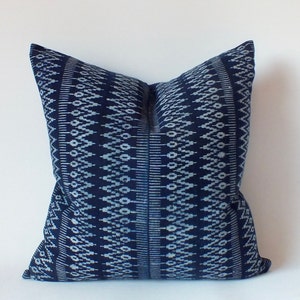 Puede incluir: Una almohada azul y blanca con un diseño geométrico. La almohada está hecha de una tela suave y tejida.