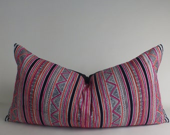 May include: A decorative lumbar pillow with a vibrant, striped pattern. The pillow features vertical stripes in black, pink, orange, and white, with embroidered geometric designs. The pillow is a long, rectangular shape.