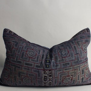 Puede incluir: Una almohada azul y blanca con un diseño geométrico. La almohada está hecha de una tela suave y tejida y tiene un borde azul oscuro.