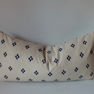 May include: A long, rectangular cushion with a white fabric cover and a navy blue geometric pattern. The pattern is a repeating design of small squares.