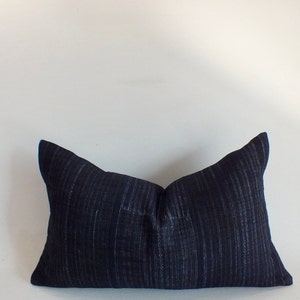 May include: A dark blue pillow with a textured fabric. The pillow is rectangular and has a slightly pointed shape at each end.