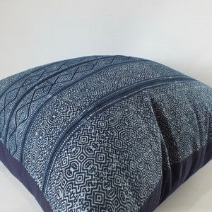 May include: A blue and white patterned cushion with a geometric design. The cushion is made of a soft, woven fabric and has a dark blue border.