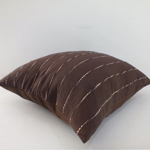 May include: A brown throw pillow with white embroidered lines. The pillow is made of a soft, textured fabric.