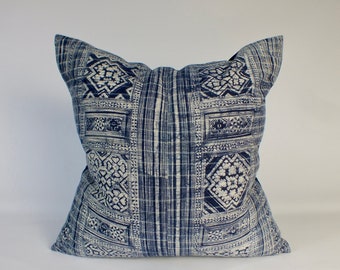 May include: Square decorative pillow with a blue and white geometric pattern. The pillow features a repeating design of squares and rectangles with floral and striped accents. The pillow is a square shape.