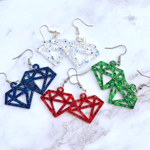 May include: Diamond-shaped dangle earrings in various colors: white, blue, red, and green. Each earring features a glittery finish and a geometric design. The earrings have silver-colored hooks for easy wear.