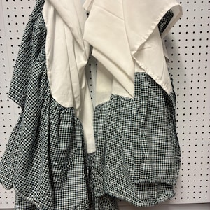 May include: Two fabric curtains featuring a dark green and white gingham check pattern on the lower portion and a solid white fabric panel on the upper portion. The curtains are gathered and draped, showing a layered design with visible folds.