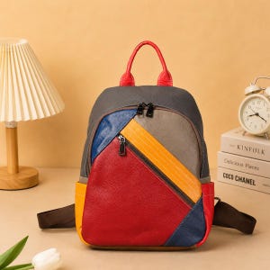 May include: A multi-colored leather backpack with a red handle and accents. The backpack features a patchwork design with red, yellow, blue, and gray panels. It has a zippered front pocket and adjustable straps.