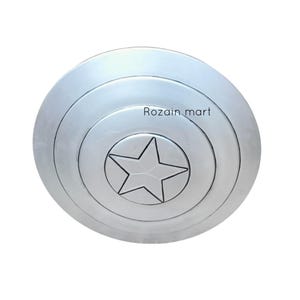 May include: A silver-colored, circular shield with concentric rings and a central star design. The shield has a metallic finish and the text "Rozain mart" is visible on the surface.