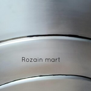 May include: A silver-colored, circular shield with a black star emblem. The shield has a brushed metal finish and the text "Rozain mart" is printed on the surface. The shield is likely a decorative item.