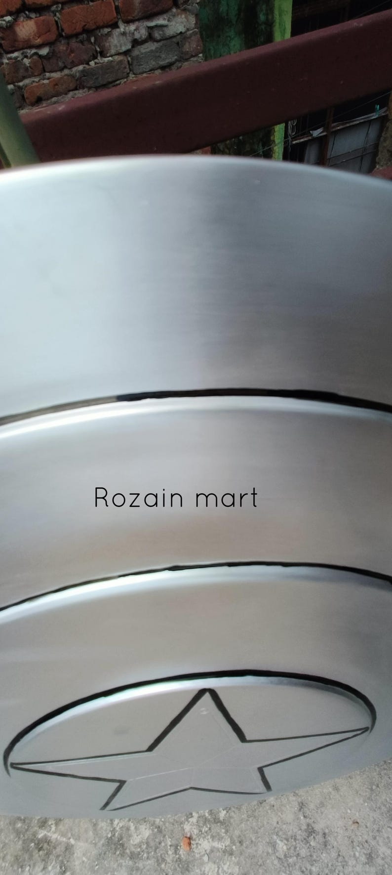 May include: A silver-colored, circular shield with a black star emblem. The shield has a brushed metal finish and the text "Rozain mart" is printed on the surface. The shield is likely a decorative item.