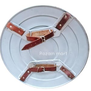 May include: A light gray, circular shield with concentric circles and brown leather straps and buckles on the back. The shield has a metallic appearance and the text "Rozain mart" is visible.