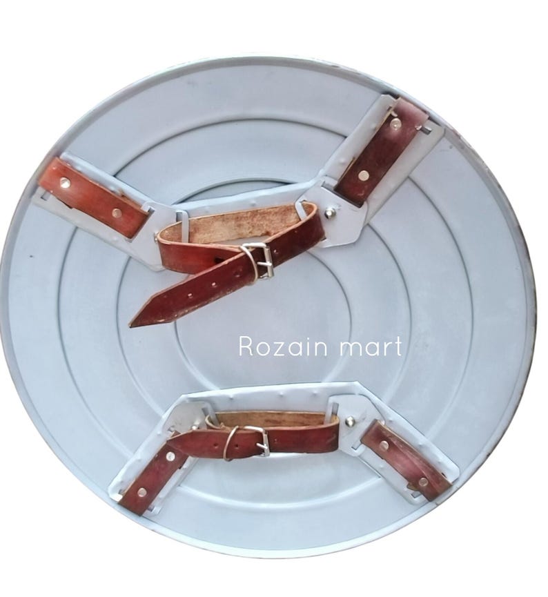 May include: A light gray, circular shield with concentric circles and brown leather straps and buckles on the back. The shield has a metallic appearance and the text "Rozain mart" is visible.