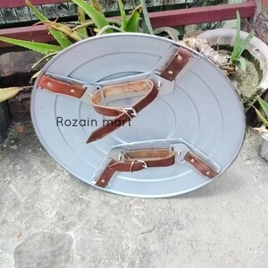 May include: A gray, circular shield with brown leather straps and buckles. The shield has a metallic appearance and features the text "Rozain mart". The straps are riveted to the shield, suggesting a durable construction.