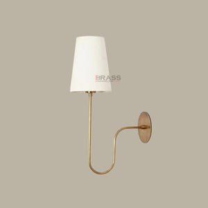 May include: A wall-mounted lamp with a white lampshade and a brass-colored metal frame. The lamp has a curved arm and a circular base. The text "BRASS CHANDELIER" is printed on the lampshade. This fixture is suitable for home decor.