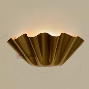 Könnte beinhalten: Eine goldfarbene Wandleuchte mit einem gerüschten, blütenblattartigen Design. Die Leuchte strahlt ein warmes Licht aus. Der Text "BRASS CHANDELIER" ist unten links sichtbar. Ein dekoratives Beleuchtungselement.