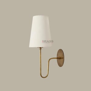 Peut inclure: Une applique murale avec un abat-jour blanc et une monture en métal couleur laiton. La lampe a un bras incurvé et une base circulaire. Le texte "BRASS CHANDELIER" est visible sur l'abat-jour. Idéale pour l'éclairage intérieur.