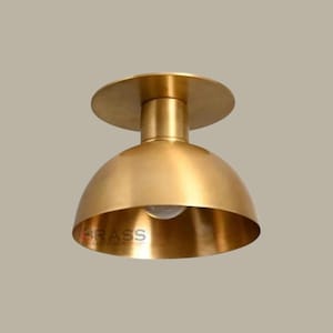 May include: A brass ceiling light fixture with a dome-shaped shade and a circular base. The fixture has a warm, golden finish and a visible light bulb. The text "BRASS CHANDELIER LAMP" is printed on the shade.
