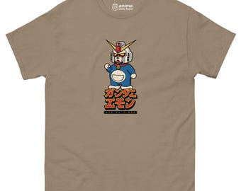 May include: A tan t-shirt with a cartoon illustration of a Gundam robot character in a blue and white outfit. Japanese text is below the character. The shirt has a crew neck and short sleeves.