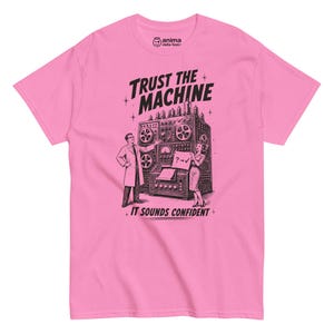 Può includere: Una t-shirt rosa acceso a maniche corte con una stampa grafica nera di un computer vintage, con una persona in camice da laboratorio e una persona in abito accanto. Il testo recita TRUST THE MACHINE e IT SOUNDS CONFIDENT.