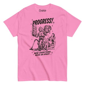 Può includere: Una t-shirt rosa brillante a maniche corte con un'illustrazione grafica nera di un robot che svolge faccende domestiche mentre una persona siede su una sedia. Il testo recita PROGRESS! e NOW EVERYTHING NEEDS AN UPDATE, con il marchio anima.